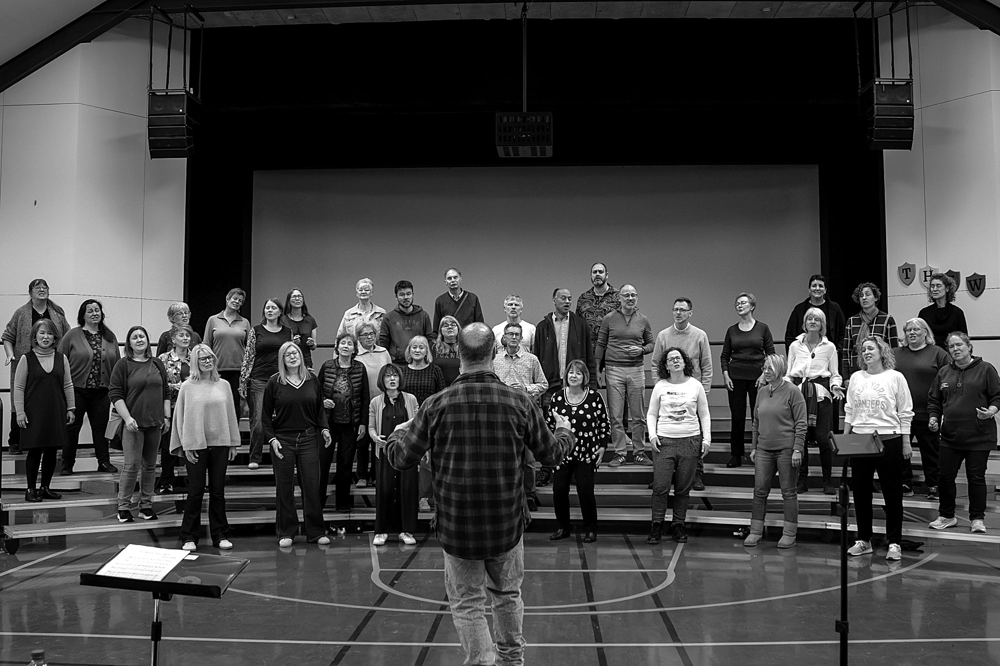The chorus singing on risers at a rehearsal with the director in front